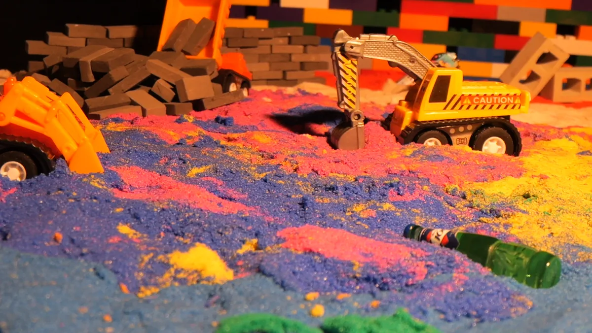 Toy excavator working through vivid colored sand